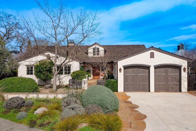 view of front of home featuring driveway, a garage, a chimney, and stucco siding