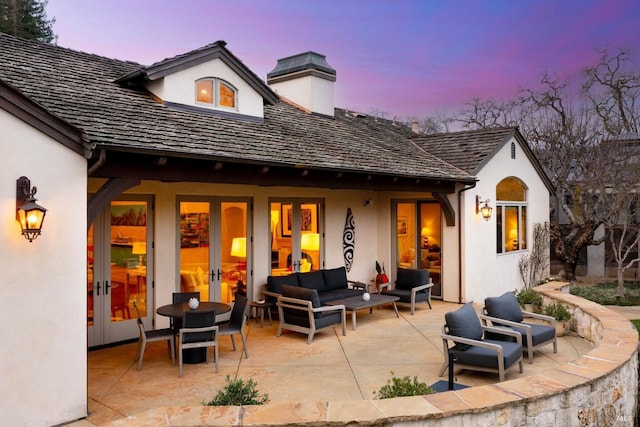 back of property at dusk with a patio, french doors, an outdoor living space, and stucco siding