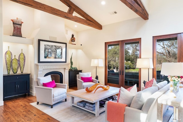 living area featuring high vaulted ceiling, a fireplace, wood finished floors, visible vents, and beamed ceiling