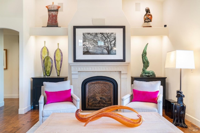 living area featuring arched walkways, a fireplace, baseboards, and wood finished floors