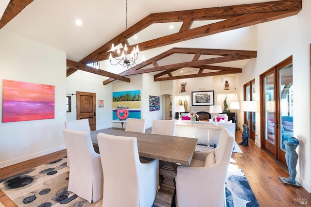 dining area with a chandelier, a fireplace, beamed ceiling, and light wood-style flooring