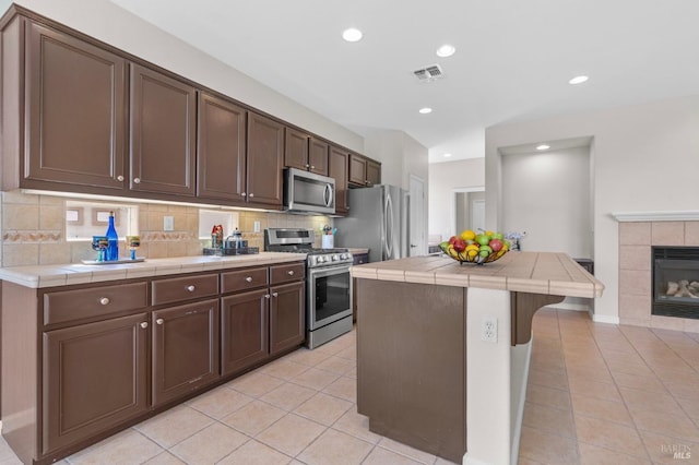 kitchen with visible vents, tile counters, decorative backsplash, stainless steel appliances, and a fireplace