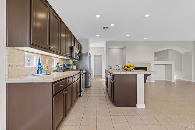 kitchen featuring dark brown cabinetry, visible vents, decorative backsplash, appliances with stainless steel finishes, and a sink