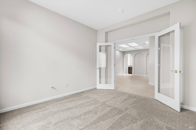 spare room with baseboards, arched walkways, light colored carpet, french doors, and light tile patterned flooring
