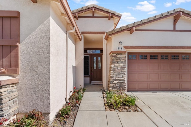 entrance to property with a garage, stone siding, a tiled roof, and stucco siding
