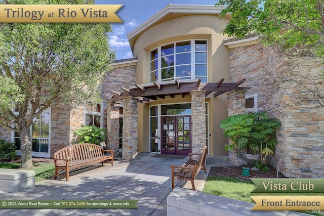 view of exterior entry with stone siding, french doors, a pergola, and stucco siding