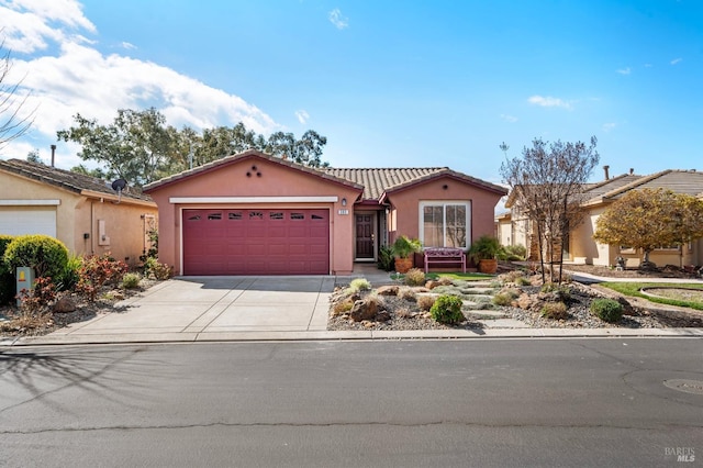 view of front of home with a garage, a tile roof, concrete driveway, and stucco siding