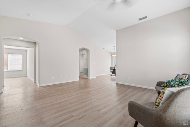 living area featuring light wood-style floors, arched walkways, visible vents, and vaulted ceiling