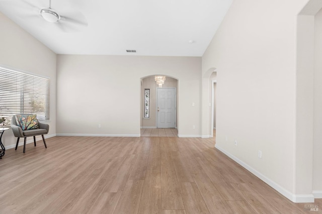 living area with arched walkways, visible vents, a ceiling fan, baseboards, and light wood finished floors