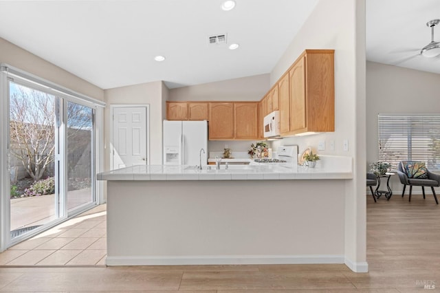 kitchen with lofted ceiling, a peninsula, white appliances, visible vents, and light wood finished floors