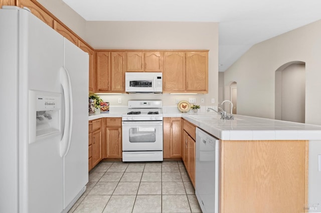 kitchen featuring light tile patterned flooring, a peninsula, white appliances, a sink, and tile counters