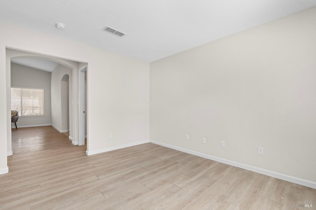 unfurnished room featuring arched walkways, baseboards, visible vents, and light wood finished floors