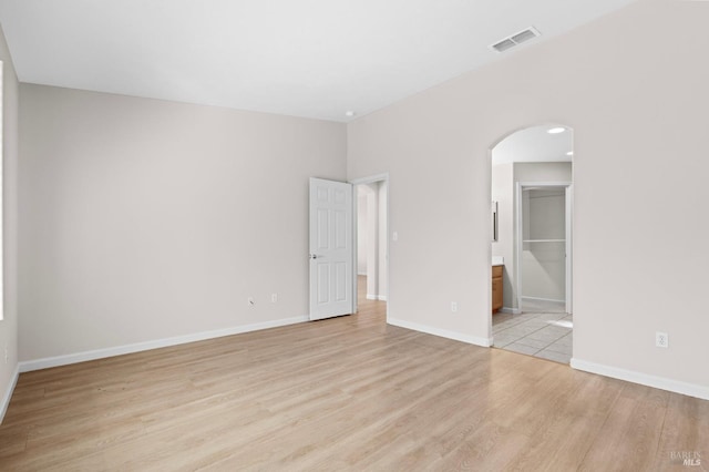 spare room with light wood-type flooring, baseboards, visible vents, and arched walkways