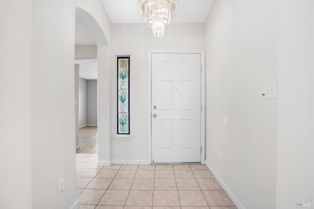 foyer entrance with light tile patterned floors, baseboards, arched walkways, and a chandelier