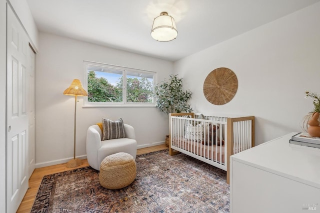 bedroom featuring a crib, a closet, baseboards, and wood finished floors