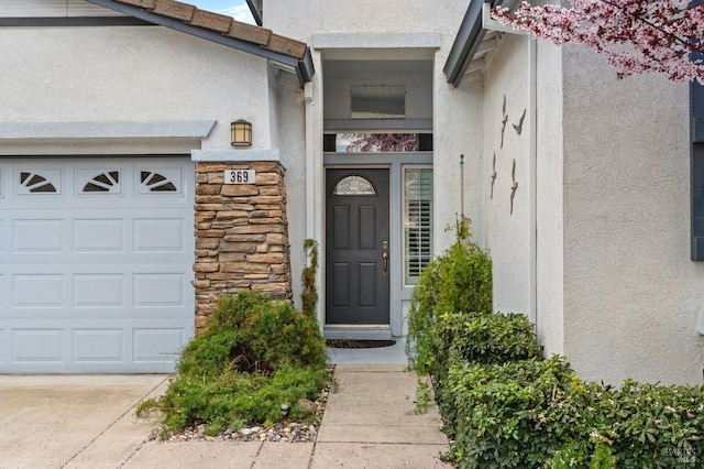 entrance to property with stone siding, an attached garage, and stucco siding