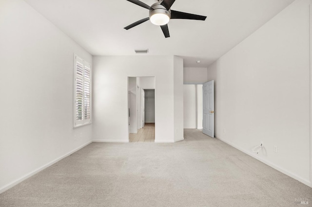 unfurnished bedroom with a walk in closet, visible vents, light carpet, and baseboards