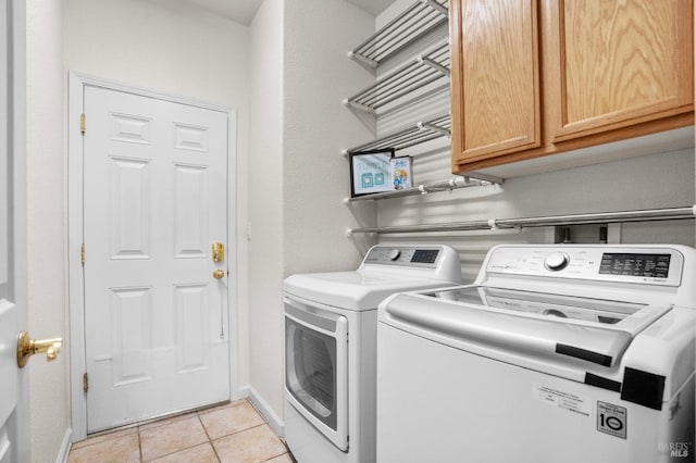 clothes washing area with cabinet space, light tile patterned floors, baseboards, and washer and dryer