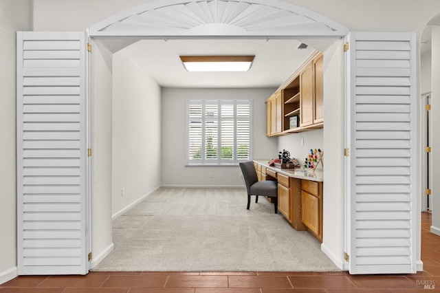 office featuring light carpet, baseboards, arched walkways, and built in study area