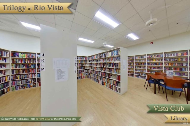 living area with wall of books, wood finished floors, and a paneled ceiling