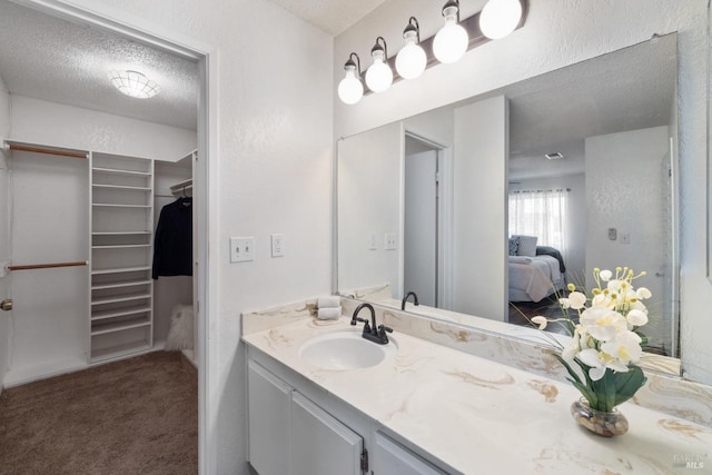 ensuite bathroom featuring a walk in closet, a textured ceiling, ensuite bath, and vanity