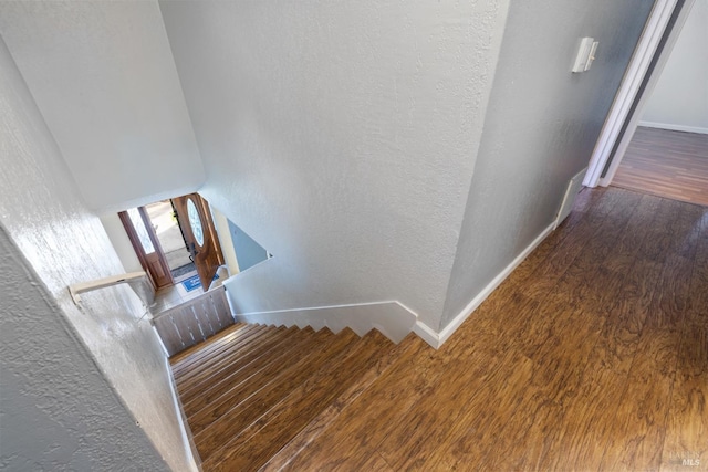 stairway with a textured wall, baseboards, and wood finished floors