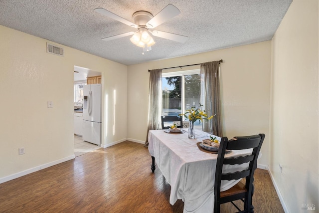 dining area with visible vents, baseboards, a ceiling fan, light wood-style flooring, and a textured ceiling