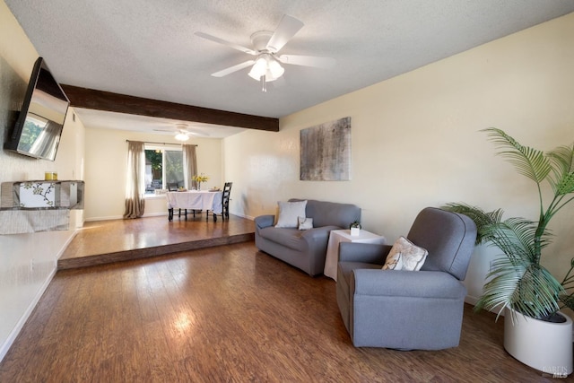 living area featuring a textured ceiling, wood finished floors, a ceiling fan, baseboards, and beamed ceiling