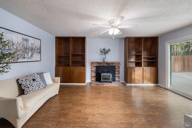 living area with a ceiling fan, a wood stove, a textured ceiling, and wood finished floors