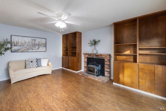 living room featuring baseboards, ceiling fan, wood finished floors, a wood stove, and a textured ceiling