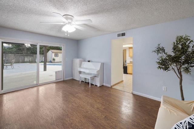 unfurnished room featuring ceiling fan, a textured ceiling, wood finished floors, visible vents, and baseboards