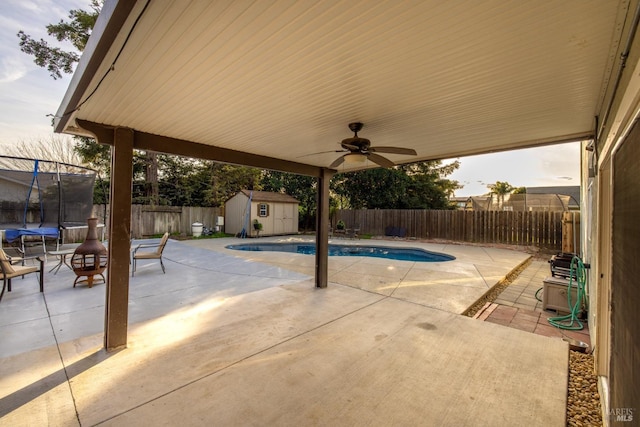 view of pool featuring a patio, a fenced backyard, an outbuilding, a trampoline, and a shed