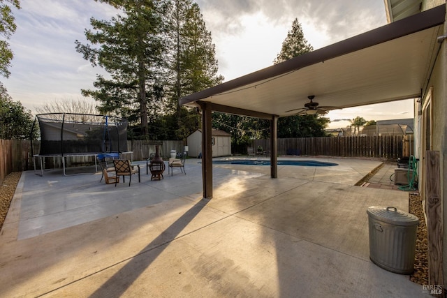 view of patio with a fenced backyard, an outdoor structure, a ceiling fan, a storage unit, and a trampoline