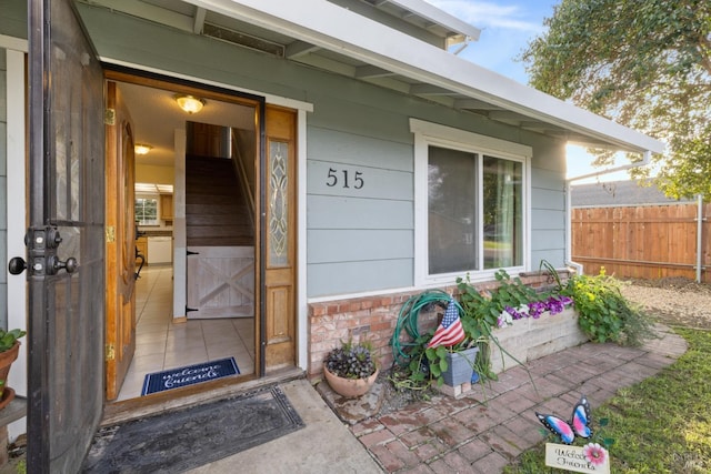 view of exterior entry featuring brick siding and fence