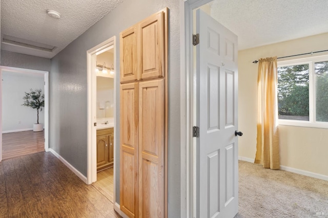 hall featuring light wood-style flooring, a textured ceiling, and baseboards