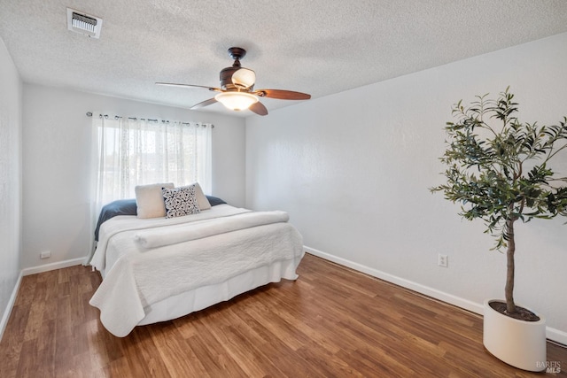 bedroom featuring a textured ceiling, ceiling fan, wood finished floors, visible vents, and baseboards