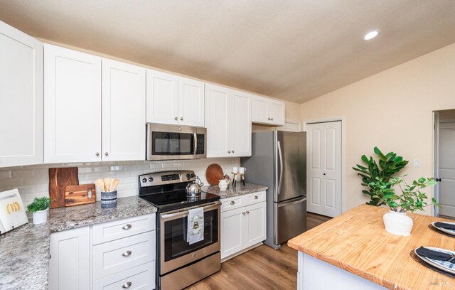 kitchen featuring stainless steel appliances, light wood-style floors, vaulted ceiling, white cabinets, and decorative backsplash