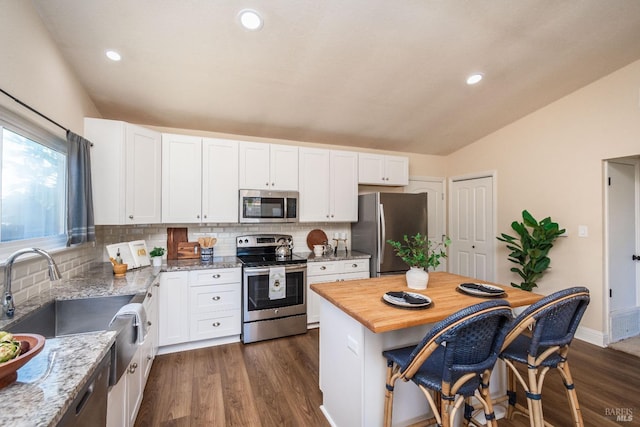 kitchen with appliances with stainless steel finishes, white cabinetry, vaulted ceiling, and a breakfast bar area