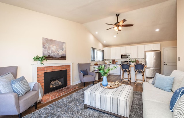 living area with recessed lighting, wood finished floors, a ceiling fan, vaulted ceiling, and a brick fireplace