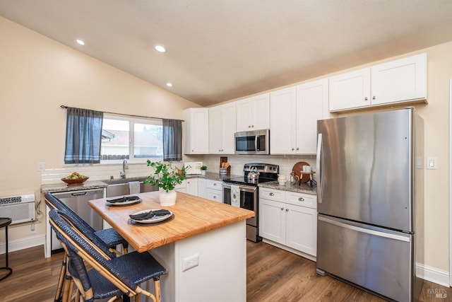 kitchen with a breakfast bar area, stainless steel appliances, decorative backsplash, white cabinets, and vaulted ceiling