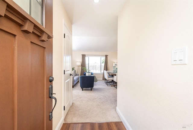 hall featuring lofted ceiling, carpet, baseboards, and wood finished floors