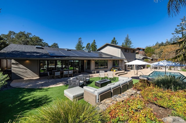 back of house with a patio, a gazebo, roof mounted solar panels, an outdoor pool, and an outdoor living space with a fire pit