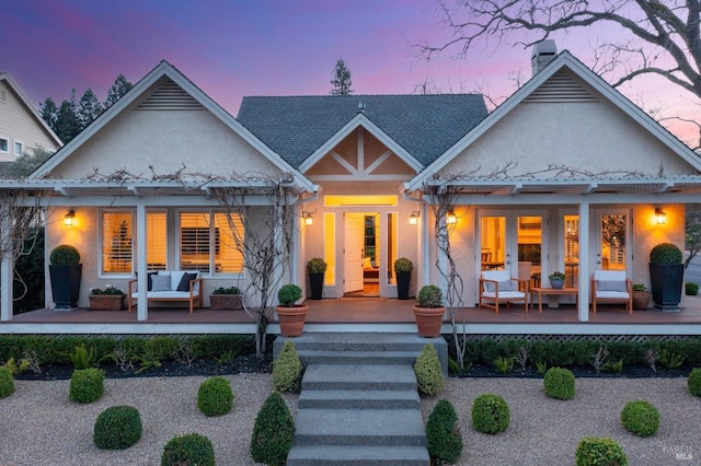 rear view of property with a shingled roof, covered porch, french doors, and stucco siding