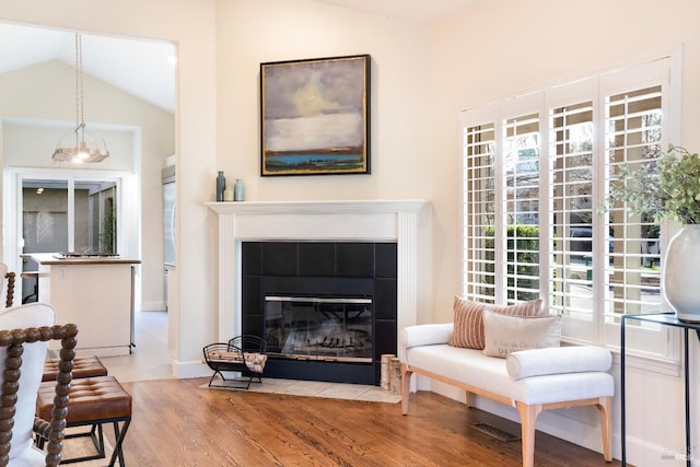 living area with lofted ceiling, a tiled fireplace, and wood finished floors