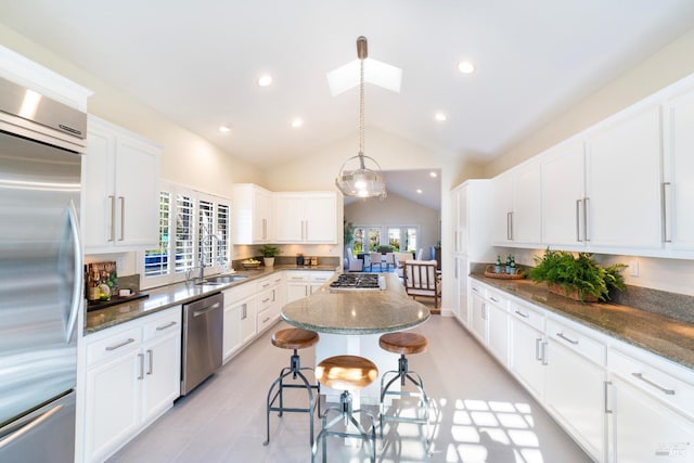 kitchen featuring appliances with stainless steel finishes, white cabinetry, a kitchen island, vaulted ceiling with skylight, and a kitchen breakfast bar