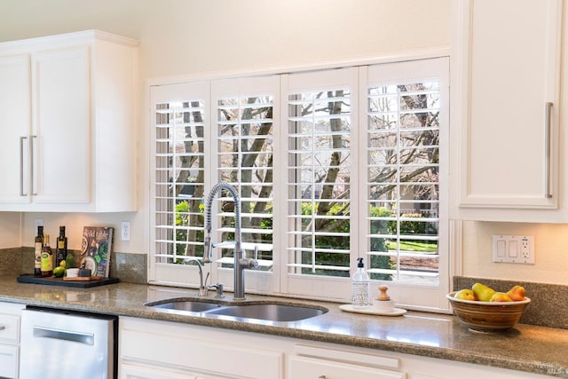 kitchen featuring dishwasher, dark stone counters, a sink, and white cabinetry