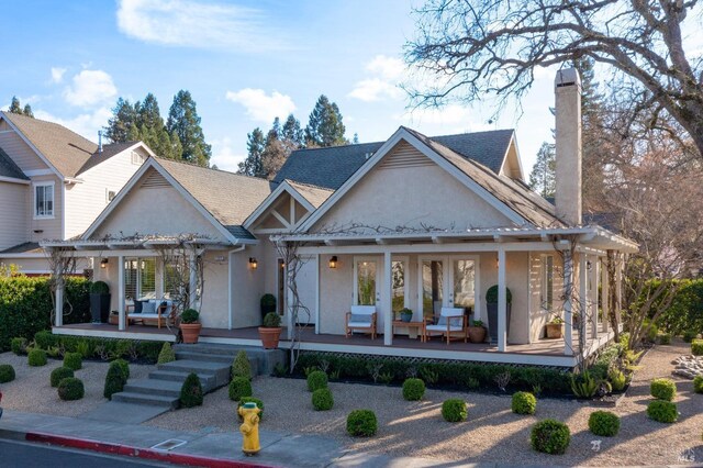 back of property featuring a chimney, covered porch, french doors, a pergola, and stucco siding