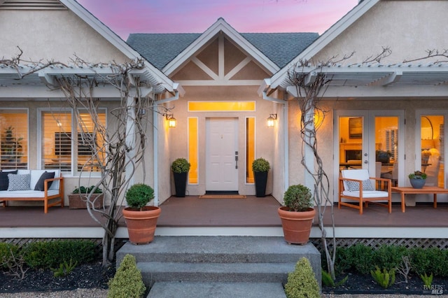 property entrance featuring covered porch, french doors, roof with shingles, and stucco siding