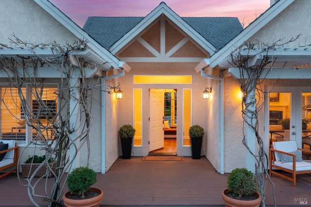 exterior entry at dusk featuring roof with shingles, french doors, and stucco siding