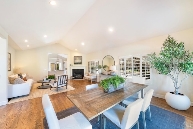 dining room with lofted ceiling, recessed lighting, a glass covered fireplace, wood finished floors, and baseboards